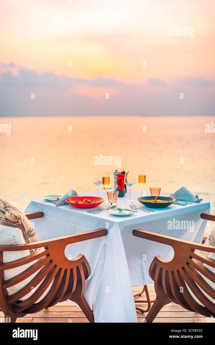 Romantischer Esstisch Sonnenuntergang mit Blick auf den Meereshimmel im Hintergrund. Liebes Paar Flitterwochen Jubiläumsfeier exklusives Ziel Dining Gourmet Essen Luxus Stockfoto