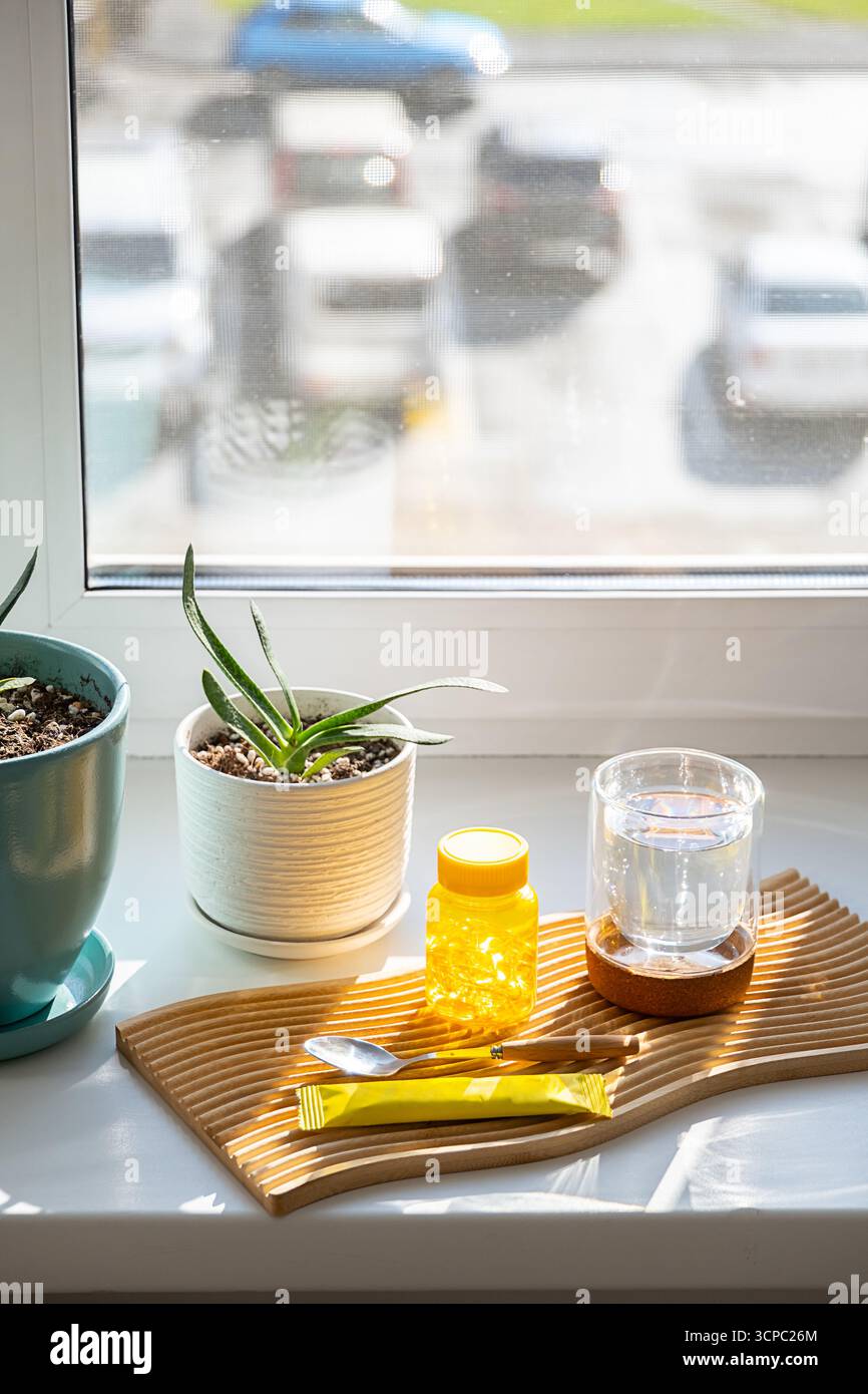 Gelbe Vitamin-D-Kapselflasche auf Holztablett mit Glas Wasser. Tägliche Ergänzung für einen gesunden Lebensstil. Wellness- und Selbstpflegekonzept. Stockfoto