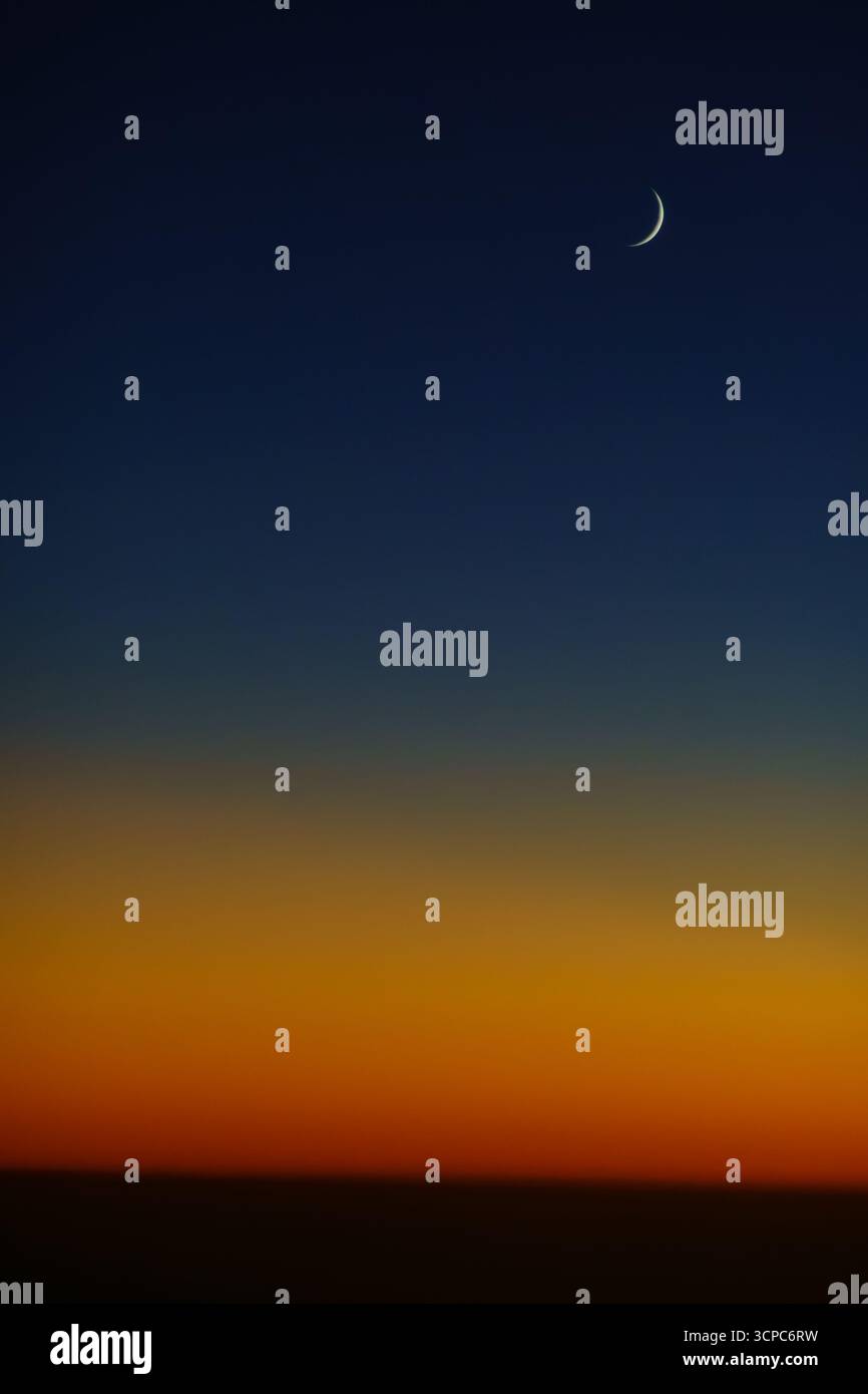 Der Halbmond hoch am dunklen Nachthimmel, über einem orangen Sonnenuntergang und der Krümmung der Erde. Aus 35.000 Metern Entfernung in einem Flugzeug. Stockfoto