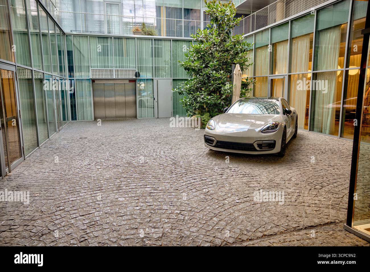 Ein eleganter silberner Porsche Panamera parkt im ruhigen Innenhof eines modernen Glasmauergebäudes in der Innenstadt von Zagreb. Stockfoto
