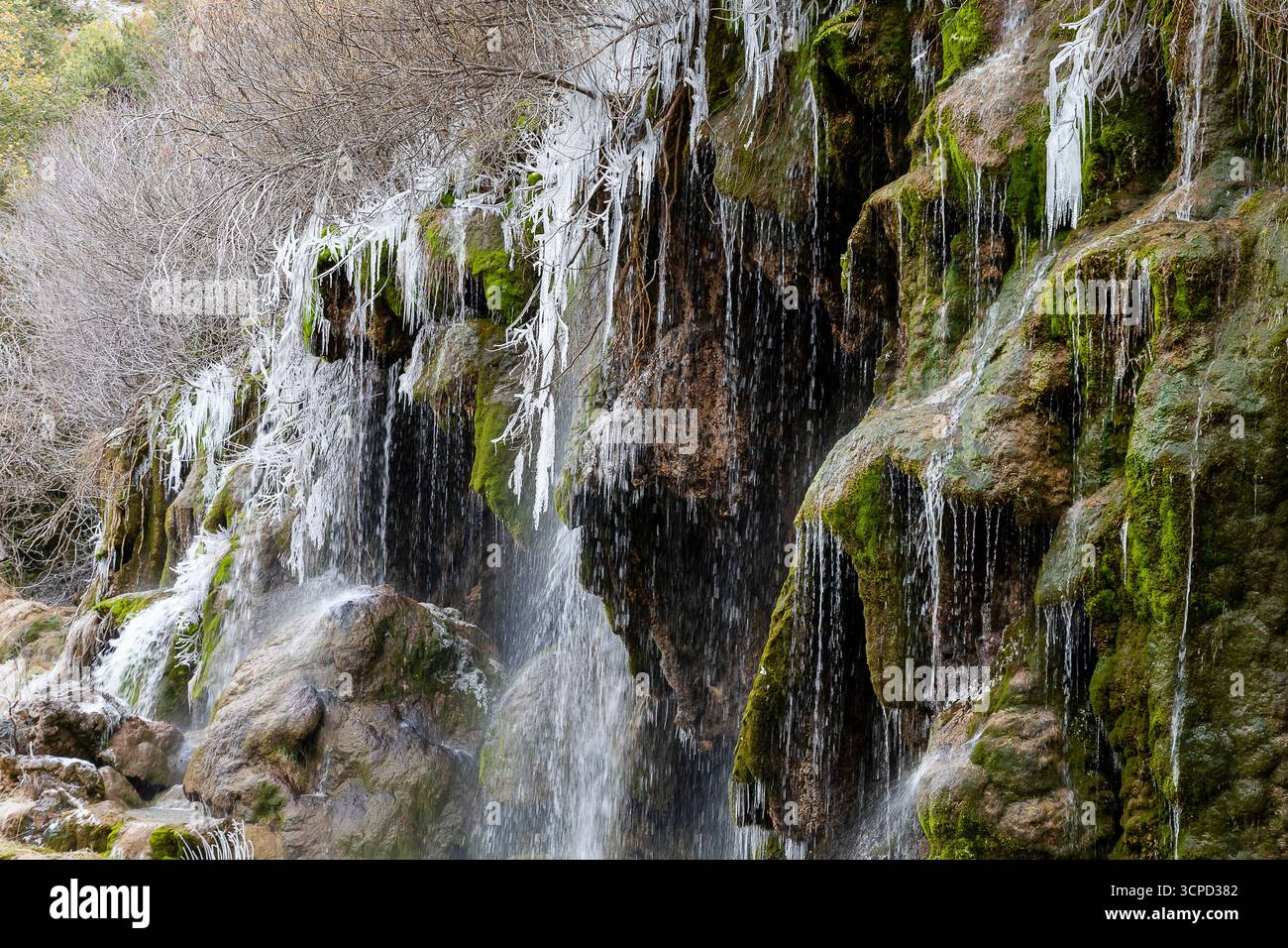 Das Wasser fließt über eine felsige Klippe, die mit Eis und üppigem grünem Moos geschmückt ist, in einer ruhigen Umgebung im Freien. Stockfoto