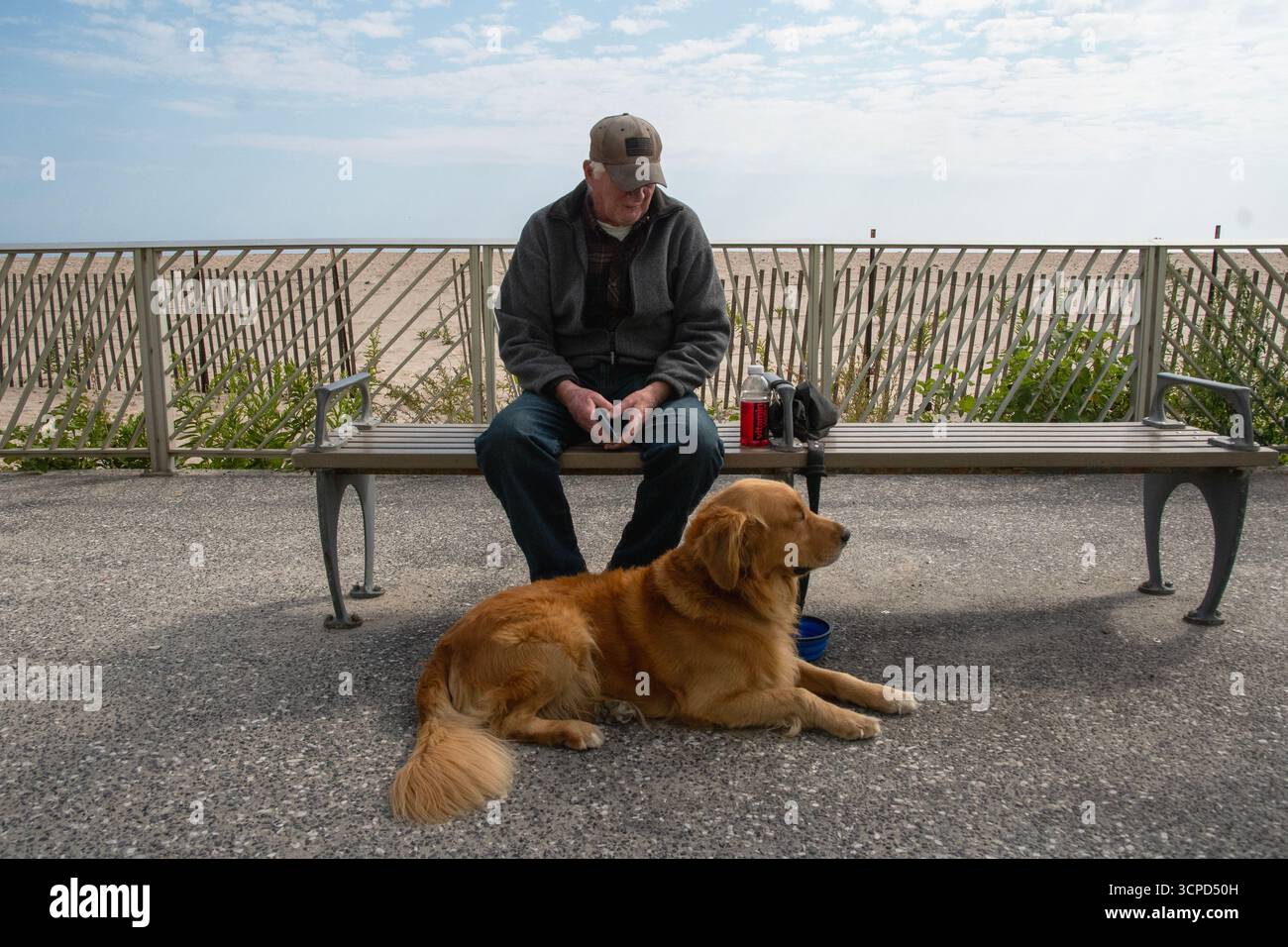 Rocky, ein goldener Retriever, der sich mit seinem Meister am Rockaway Boardwalk in Queens New York entspannt Stockfoto