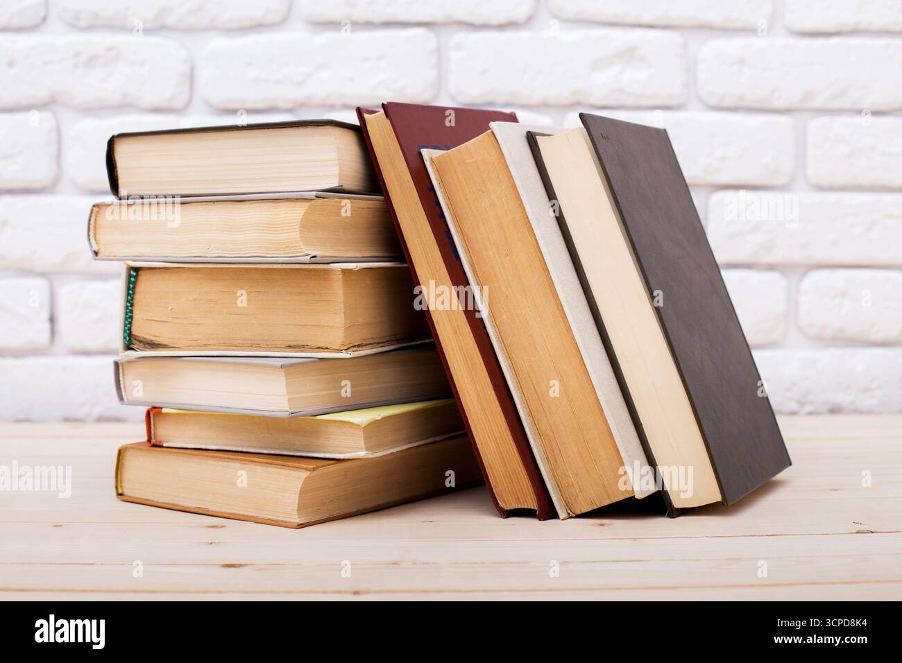 Gestapelte Bücher mit verschiedenen Einlagen, die auf einem Holztisch gegen eine Ziegelwand ruhen Stockfoto