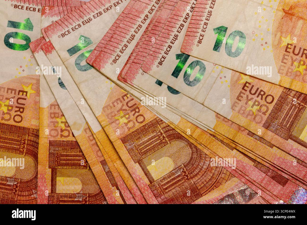 Ein Nahaufnahme, leicht abgewinkelt, von mehreren sich überschneidenden zehn-Euro-Banknoten. Vorherrschende Farben sind Gelb, Orange und Rot. Stockfoto