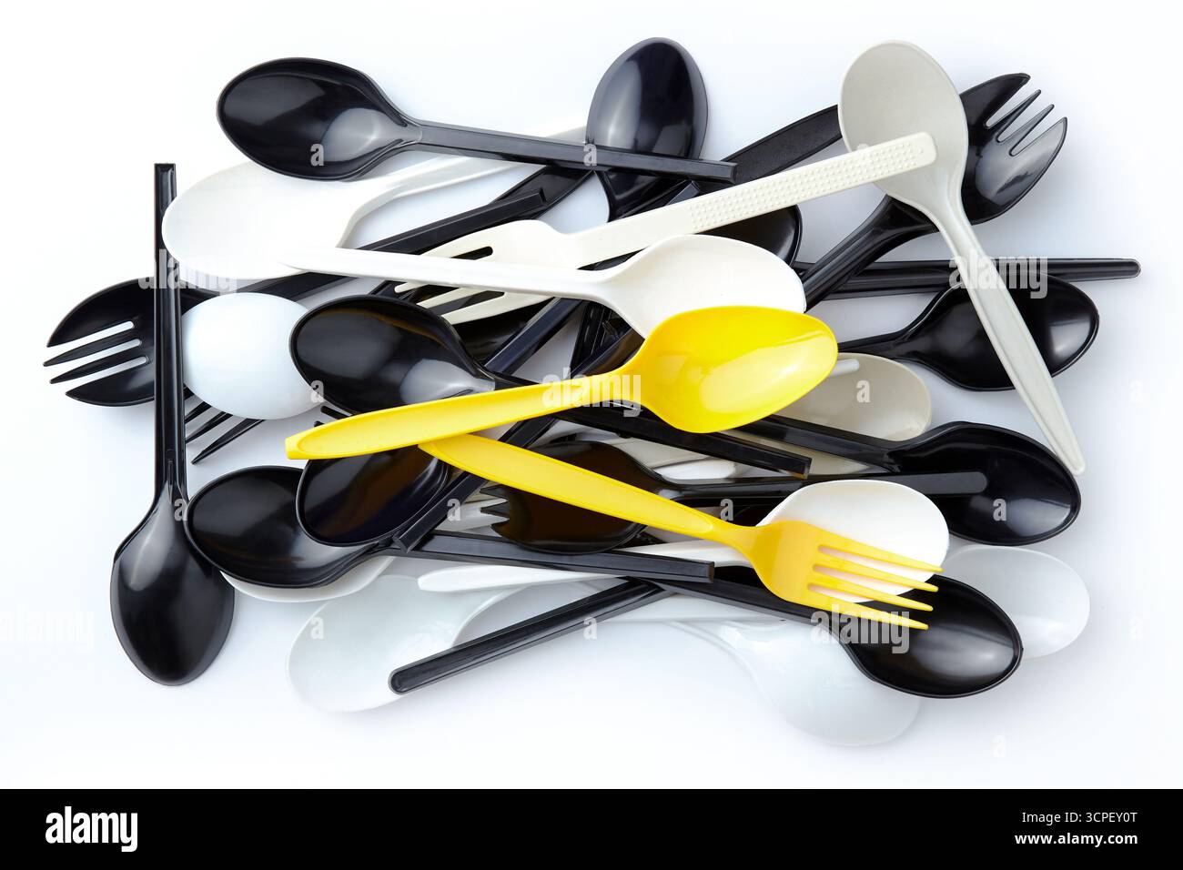 Ein Paar gelbe Kunststofflöffel und -Gabeln zwischen einem Stapel schwarz-weißer Kunststofflöffel und -Gabeln Stockfoto