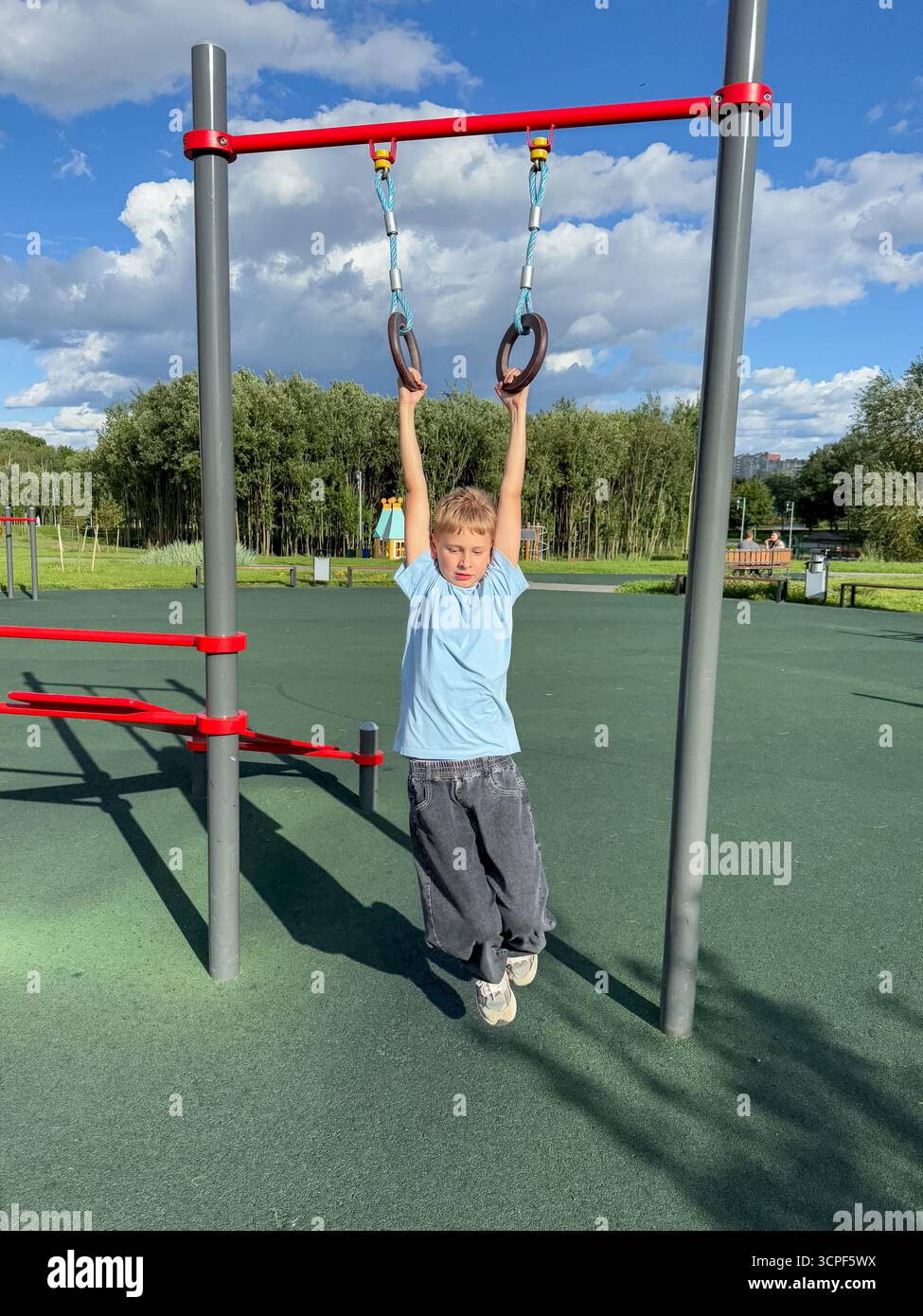 Teen Boy, der an einem hellen Sommertag auf Gymnastikringen auf einem Outdoor-Sportspielplatz trainiert, Fitness- und sportliches Aktivitätskonzept - Smartphone-aufgenommenes Stockfoto