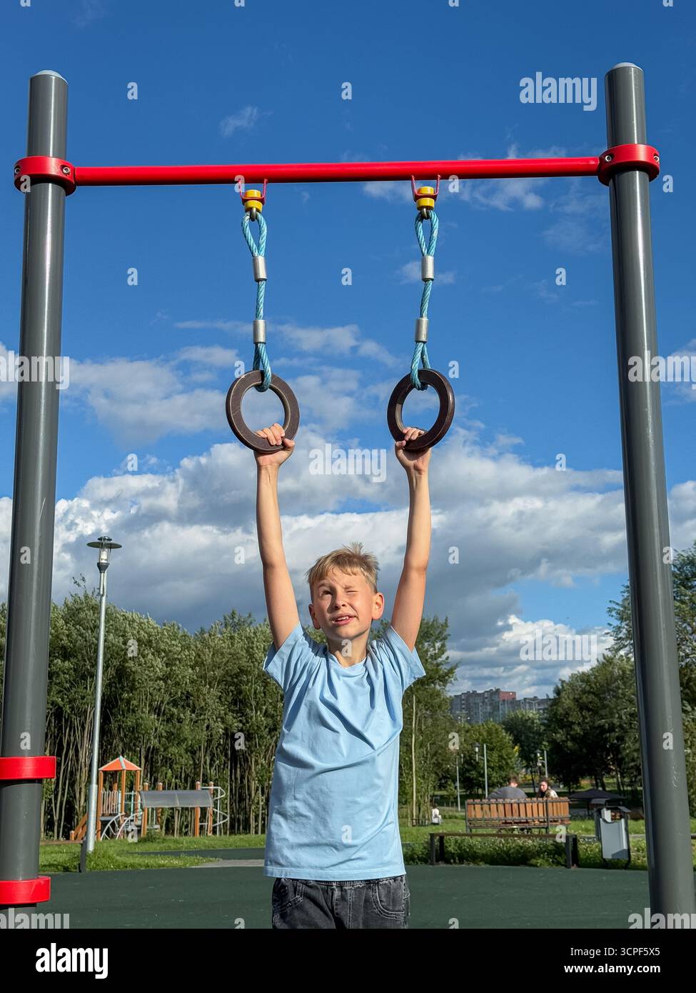 Teen Boy, der an einem hellen Sommertag auf Gymnastikringen auf einem Outdoor-Sportspielplatz trainiert, Fitness- und sportliches Aktivitätskonzept - Smartphone-aufgenommenes Stockfoto