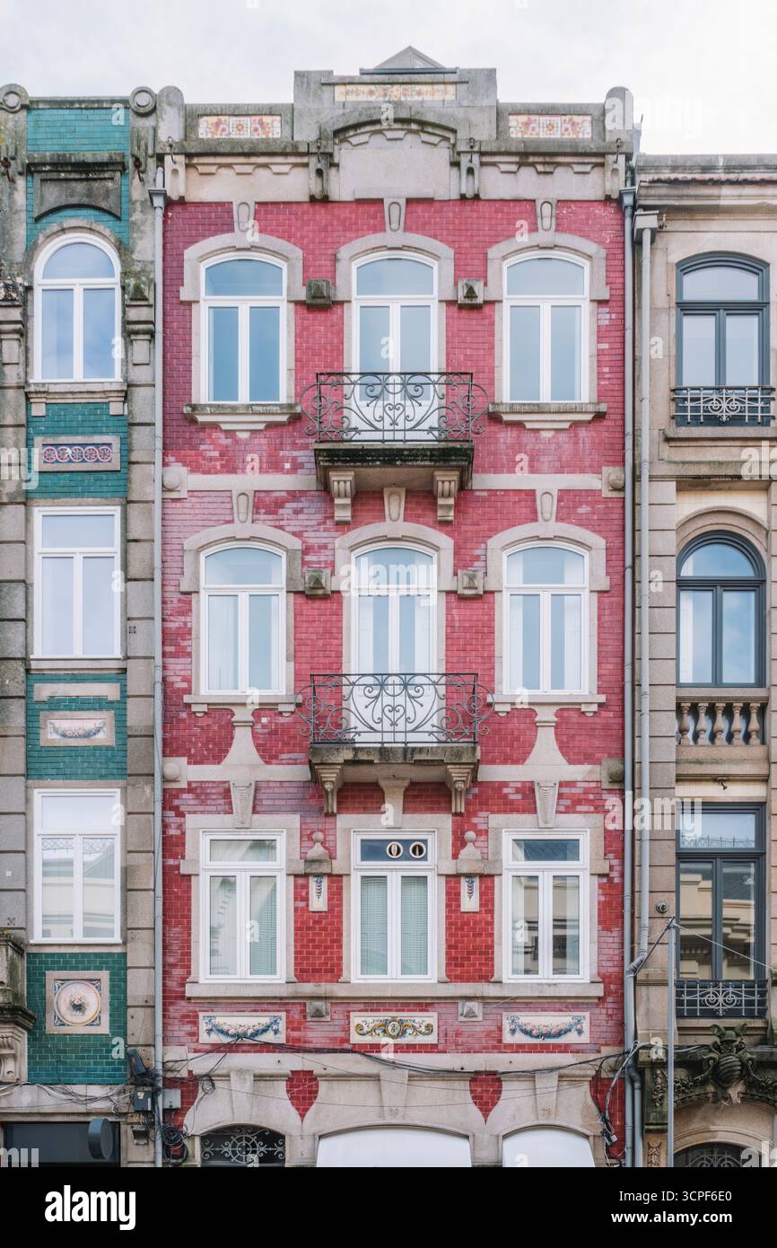 Eindrucksvolle Fassade des Porto-Gebäudes mit hellrotem Ziegelwerk und dekorativen Bogenfenstern in der historischen Innenstadt von Portugal. Traditionelle Architektur Stockfoto
