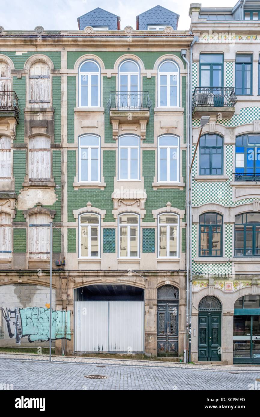Historische Fassade des Portogebäudes mit grünem Azulejo Tiling, gegenübergestellt renovierte weiße Fenster und verschlechterte Abschnitte in Portugal, Stadterneuerung Stockfoto