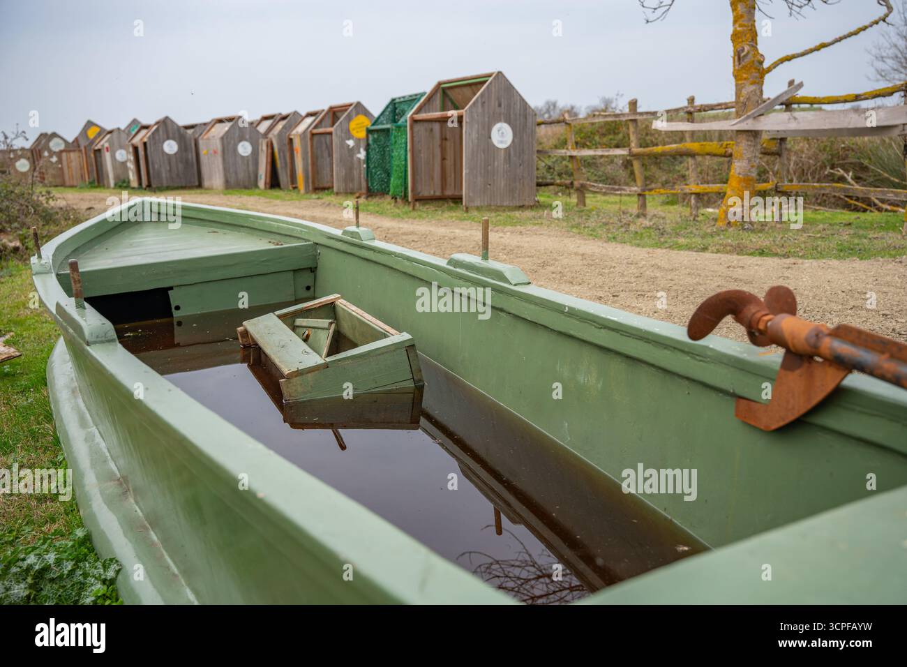Altes grünes Fischerboot mit rostigem Ruder in der Nähe des ländlichen Weges. Überflutetes grünes Holzboot, gefüllt mit Wasser, untergetaucht. Auf Dem Land Stockfoto