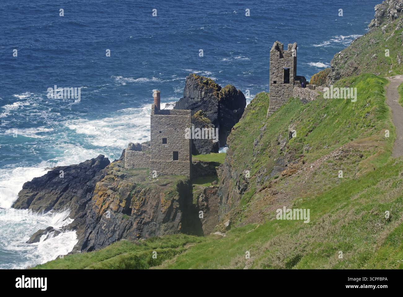 Historische Ruinen auf einer Klippe, umgeben von felsiger Küste und rauschenden Meereswellen, Maschinenraum einer alten Kupfermine in Cornwall, Großbritannien Stockfoto