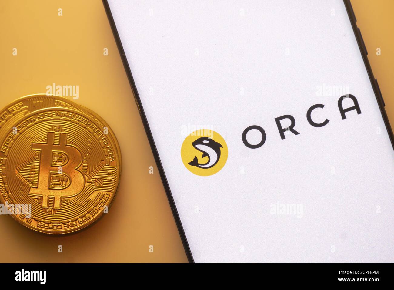 Bitcoin-Münze neben Smartphone mit Orca-Logo auf weißem Bildschirm  Stockfotografie - Alamy