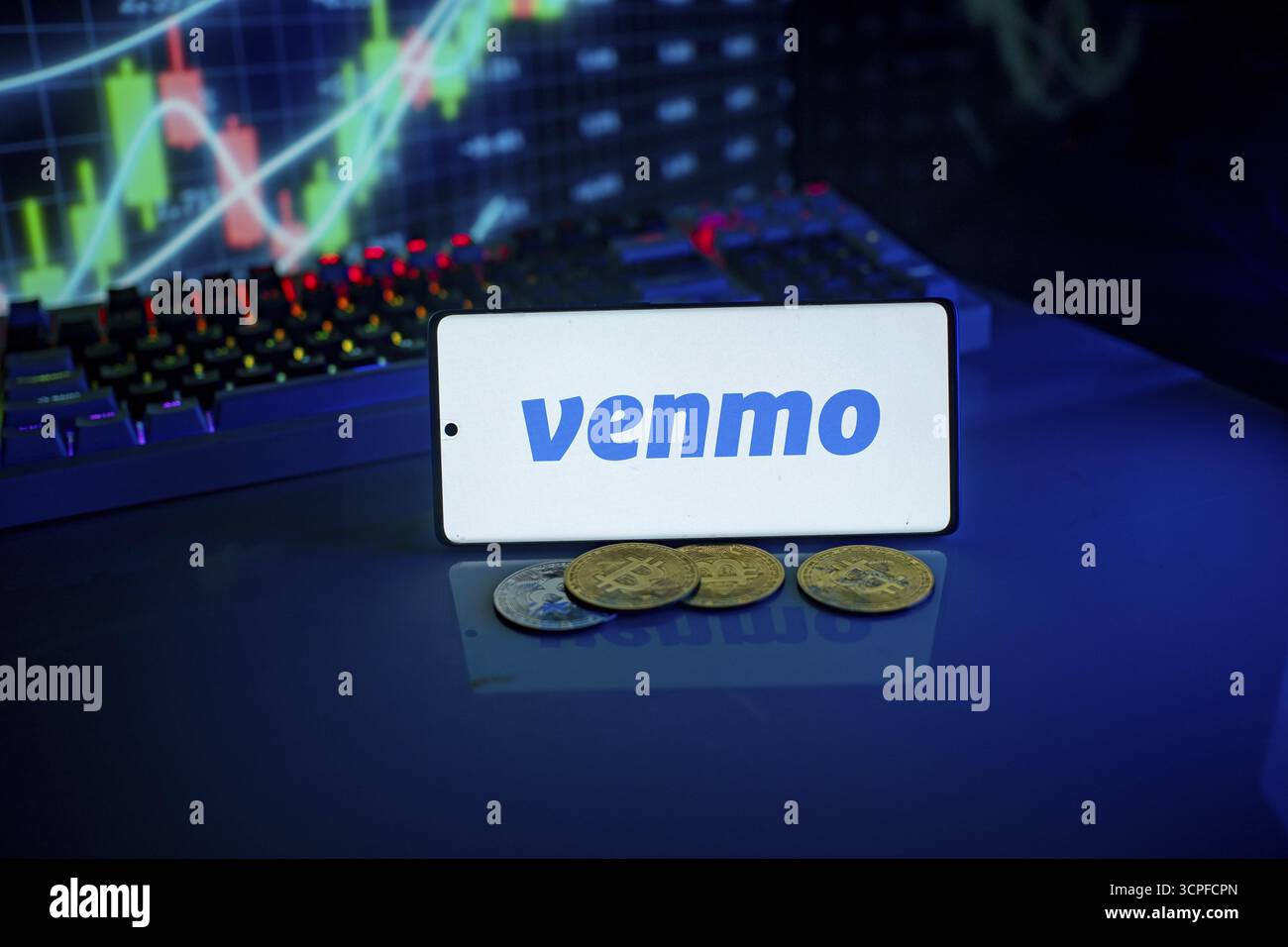 Telefon mit Venmo-Logo mit Münzen und hintergrundbeleuchteter Tastatur, die digitale Zahlungen und Finanzen anzeigt Stockfoto
