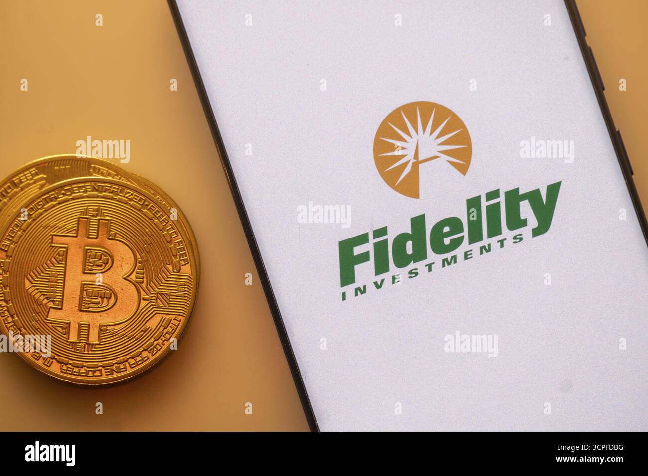 Bitcoin-Münze neben einem Smartphone mit dem Fidelity Investments Logo auf hellem Hintergrund Stockfoto
