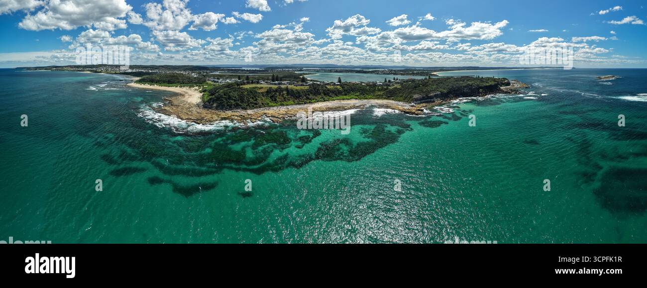 Blick aus der Vogelperspektive auf die Küste, wo türkisfarbenes Wasser auf zerklüftete, felsige Küsten trifft und üppiges Grün in Richtung Horizont, Swansea, New South Wal reicht Stockfoto