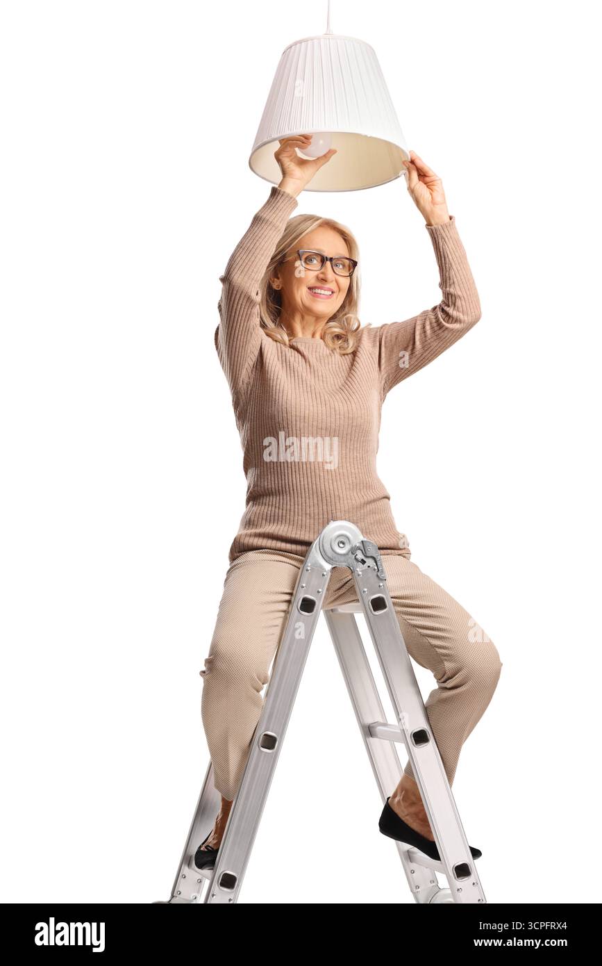 Frau, die auf einer Leiter sitzt und eine Glühbirne wechselt, isoliert auf weißem Hintergrund Stockfoto