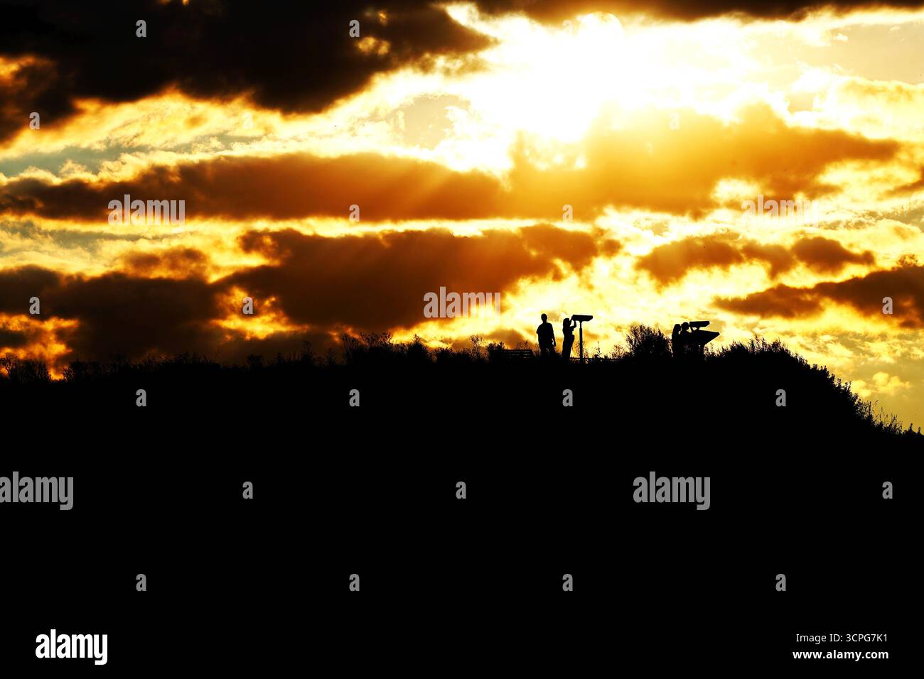 Silhouetten von Menschen auf einem Hügel mit Sonnenuntergang über Stockfoto