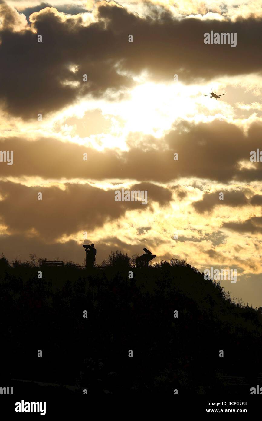 Silhouette einer Person auf einem Hügel mit majestätischem Sonnenuntergang und einem Flugzeug, das über den Hügel fliegt Stockfoto