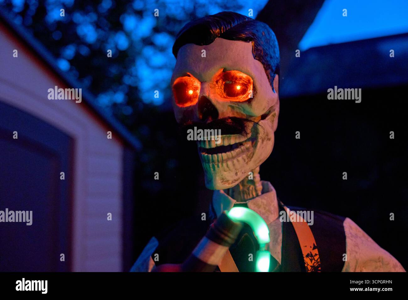 Vorderansicht eines Skelett-Barkepers mit einer Flasche und einem leuchtenden Auslauf. Rote Augen und dunkle Gartenbeleuchtung sorgen für eine gruselige Halloween-Szene. Stockfoto