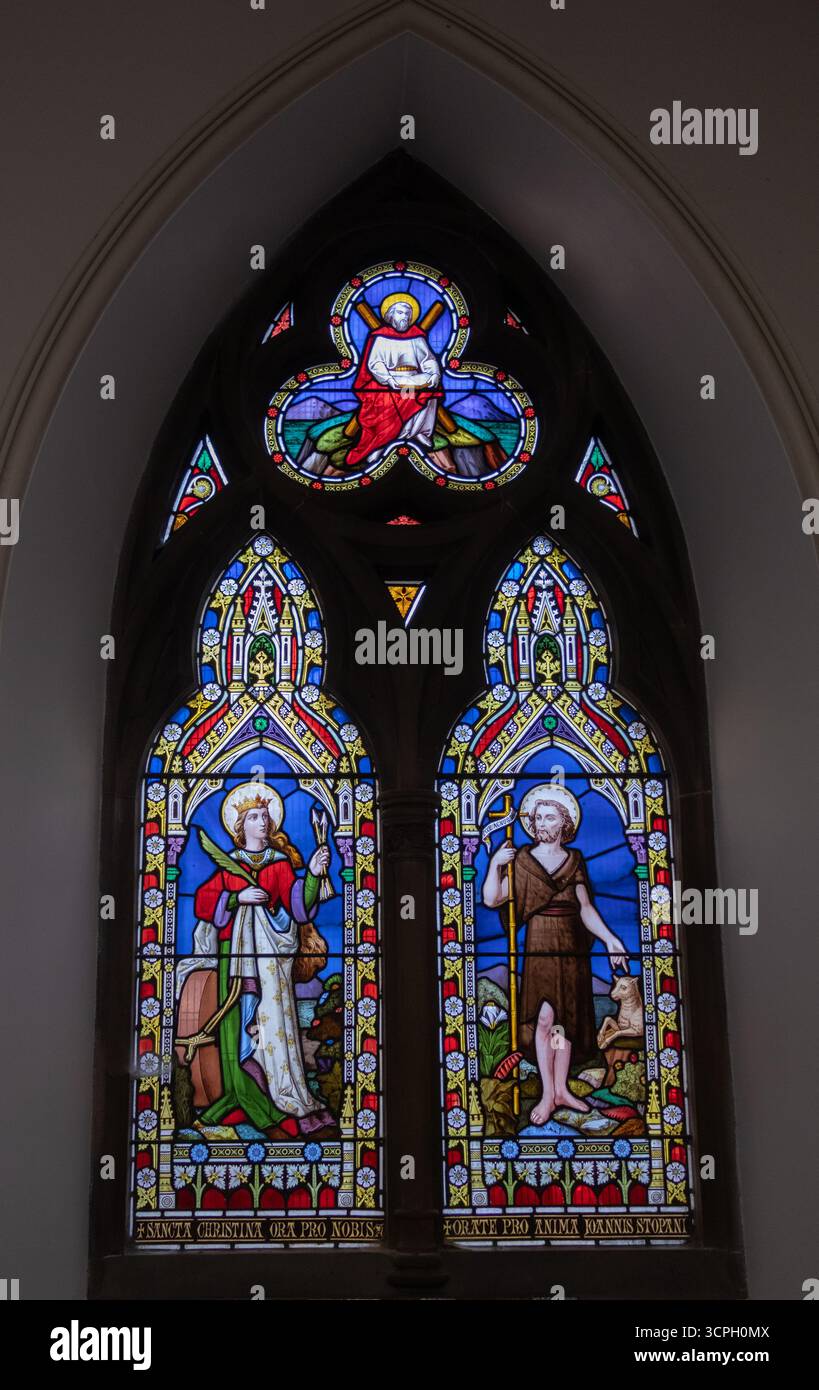 Prächtiges Buntglasfenster mit religiösen Figuren in lebhaften Farben in einem bogenförmigen architektonischen Rahmen. Stockfoto