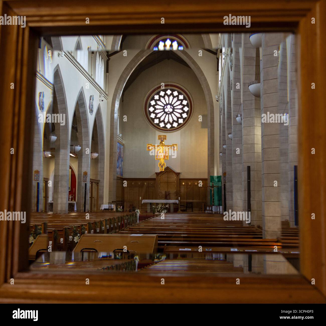 Warmes, einladendes Inneres des Alters der Heiligen Maria der Himmelfahrt mit Blick durch eine hölzerne, glasverkleidete Tür, die ein goldenes Kruzifix hervorhebt. Stockfoto