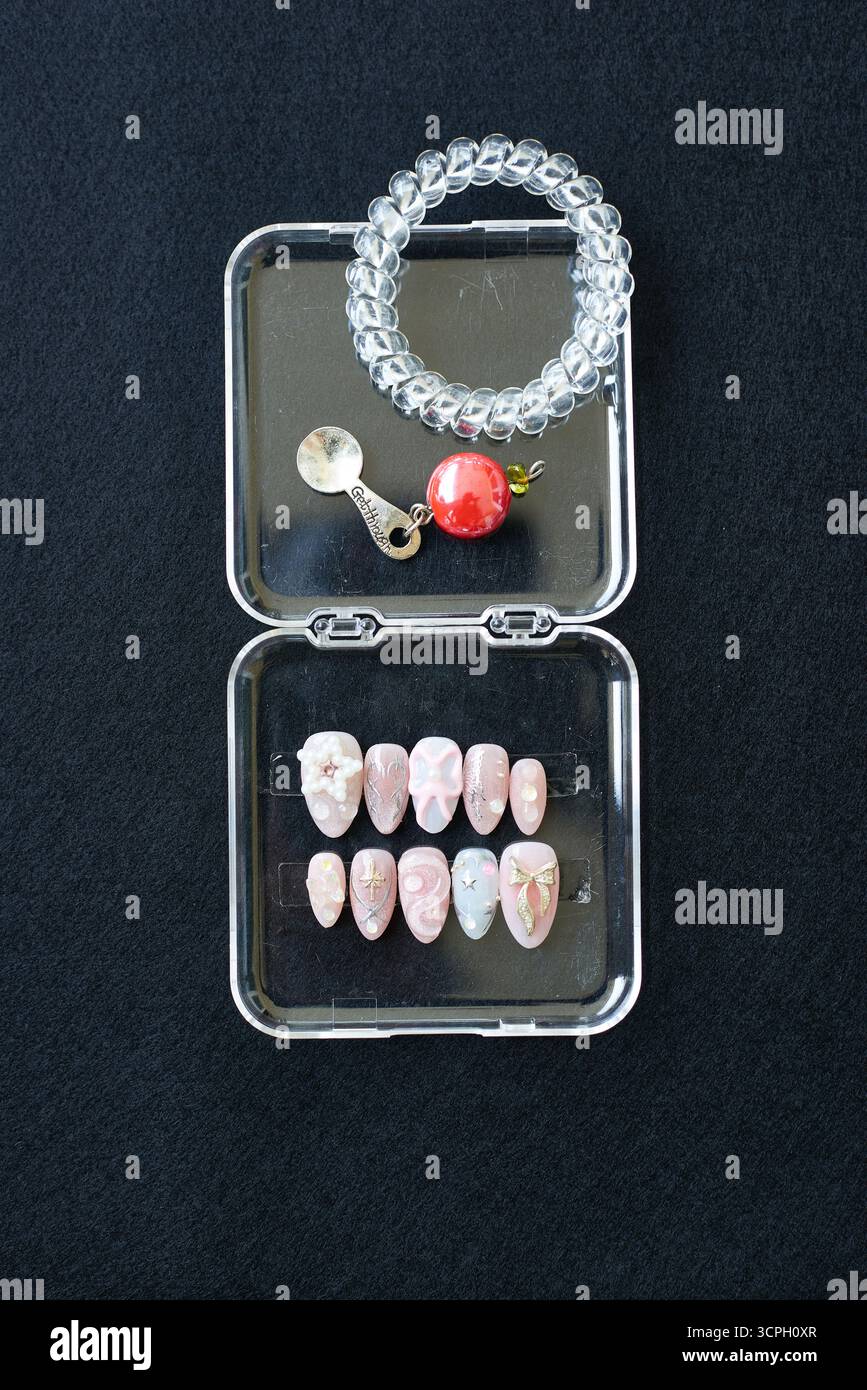 Nahaufnahme mit pastellfarbenen Nagel-Designs mit Blumen-, Stern- und Schleifendetails, mit einem klaren Armband und Anhänger auf dunklem Stoff. Ideal für Schönheit, Fashionik Stockfoto