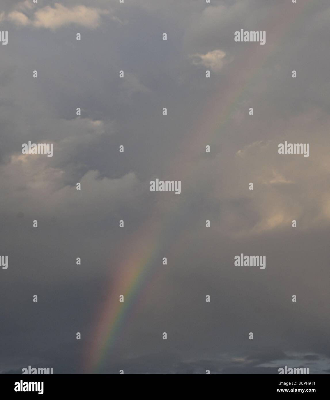 Regenbogen leuchtet hell über wolkengefüllten Himmel und offenbart eine magische Mischung aus Gelassenheit, Farbe und stimmungsvollen Geheimnissen. Stockfoto