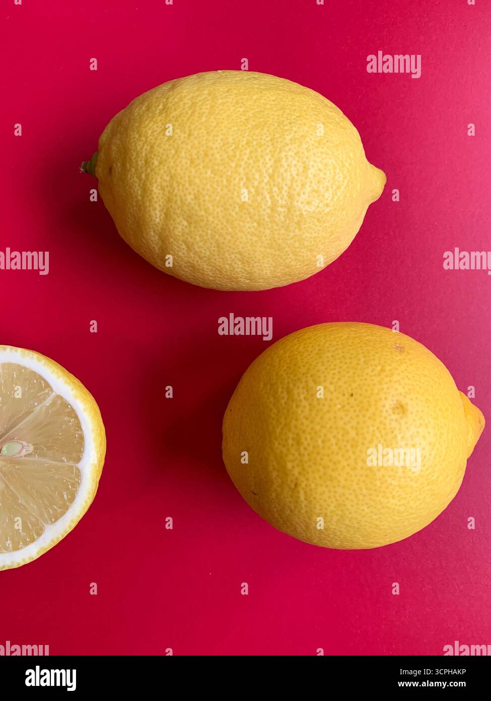 Frisches Zitronenmuster auf einem lebhaften rosa Hintergrund. Flache Lagen. Zitronen. Vitamin C. kreative Minimal Art. Minimales Sommerkonzept. Ganze und halbierte Zitrone. - Smartphone-aufgenommenes Stockfoto