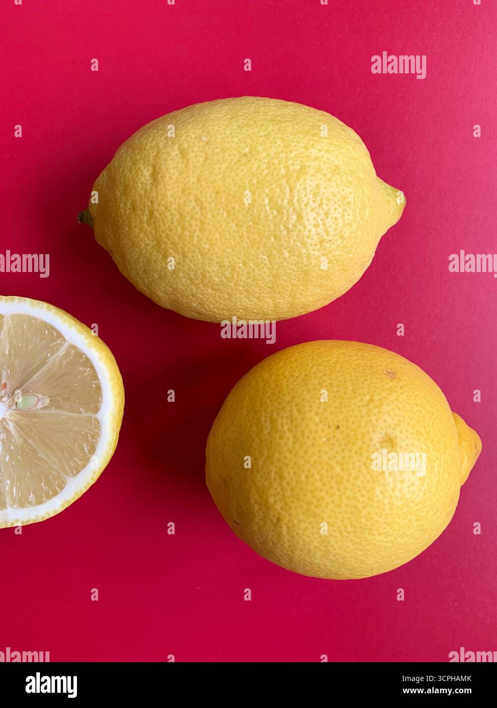 Frisches Zitronenmuster auf einem lebhaften rosa Hintergrund. Flache Lagen. Zitronen. Vitamin C. kreative Minimal Art. Minimales Sommerkonzept. Ganze und halbierte Zitrone. - Smartphone-aufgenommenes Stockfoto