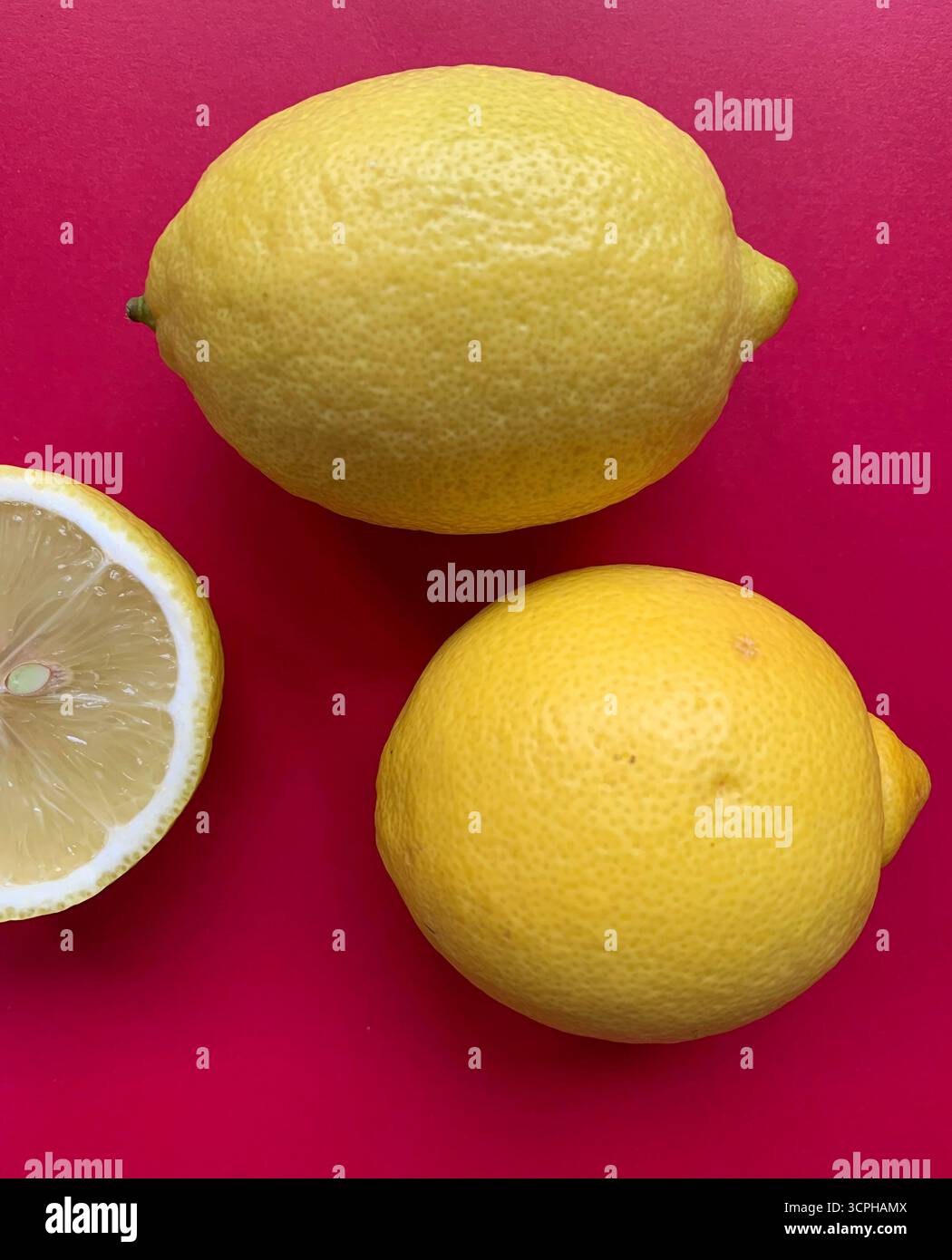 Frisches Zitronenmuster auf einem lebhaften rosa Hintergrund. Flache Lagen. Zitronen. Vitamin C. kreative Minimal Art. Minimales Sommerkonzept. Ganze und halbierte Zitrone. - Smartphone-aufgenommenes Stockfoto