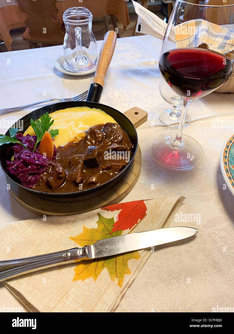 Mittagessen in Südtirol. Polenta, Fleisch und Rotwein. Italienische Küche. Reisen Sie nach Italien. Norditalien. Reise- und Tourismuskonzept. Langsames Leben. - Smartphone-aufgenommenes Stockfoto