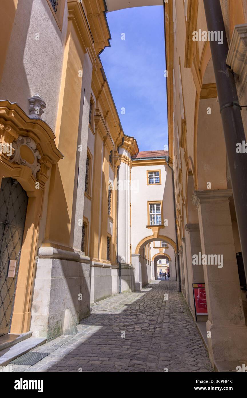 Melk, Österreich - 5. Juni 2022: Malerische Kopfsteinpflasterallee flankiert von historischen Gebäuden mit komplexen gelben Wänden unter einem hellblauen Himmel Stockfoto