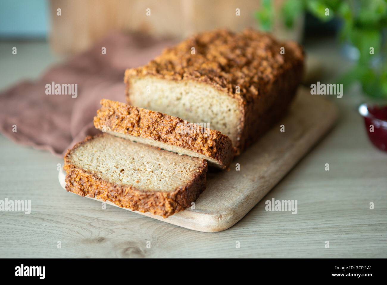 Frisch gebackenes Brot mit Vollkornbrot auf einem kleinen Holzschneidebrett. Der Brotlaib hat eine stark strukturierte, rustikale Kruste und eine weiche Innenseite Stockfoto