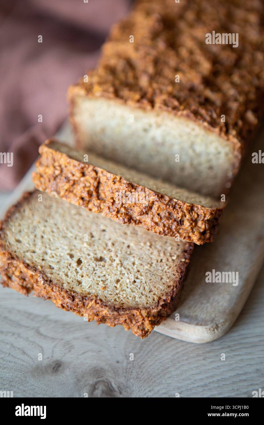Frisch gebackenes Brot mit Vollkornbrot auf einem kleinen Holzschneidebrett. Der Brotlaib hat eine stark strukturierte, rustikale Kruste und eine weiche Innenseite Stockfoto