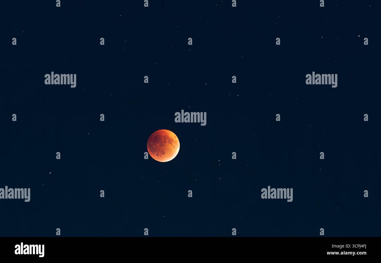 Dieses fesselnde Bild zeigt einen Blutmond, der den Nachthimmel beleuchtet, umgeben von funkelnden Sternen, die ein Gefühl von Staunen und kosmischer Schönheit wecken Stockfoto