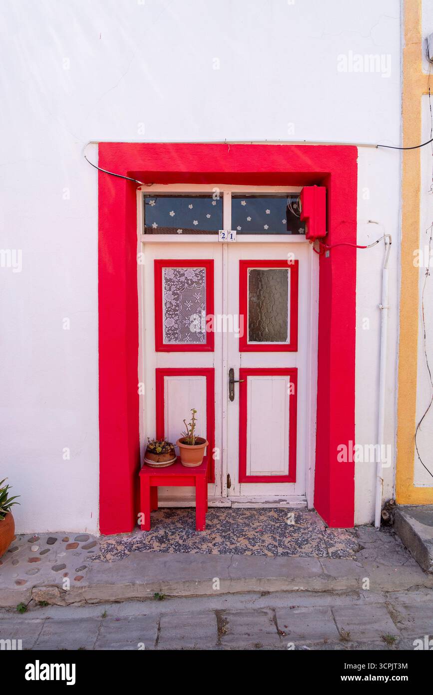 Eine hellrote Tür, die von einer weißen Wand eingerahmt wird, ist mit Topfpflanzen am Eingang dekoriert. Diese charmante Tür vermittelt die ganze künstlerische Atmosphäre. Stockfoto