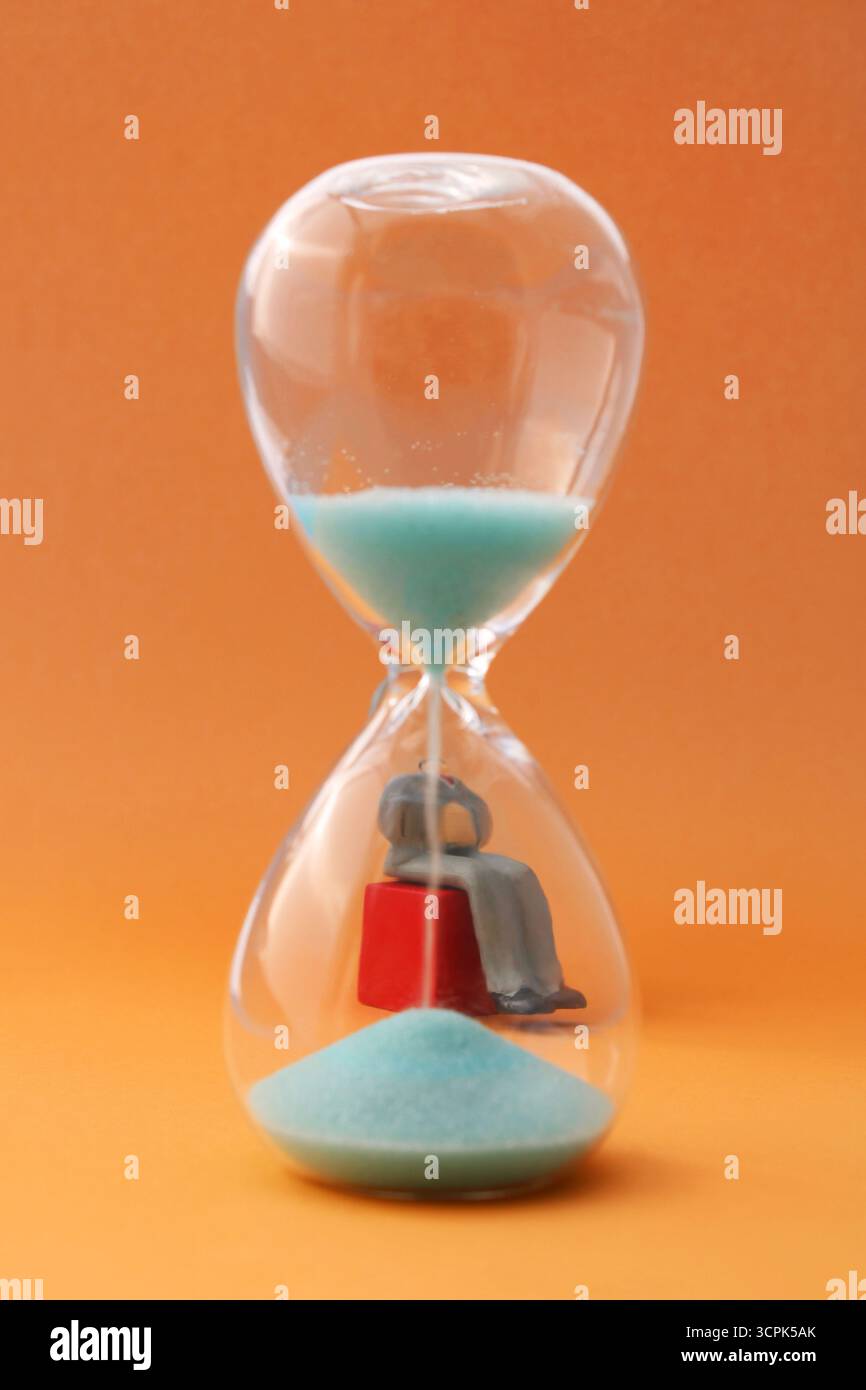 Der Executive lässt die Zeit vergehen, indem er hinter einer Sanduhr sitzt Stockfoto