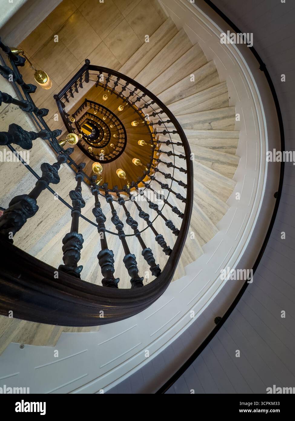 Wendeltreppe mit kunstvollem Eisengeländer und warmen Hängeleuchten von oben schaffen dramatische architektonische Perspektive und elegante historische Atmosphäre Stockfoto