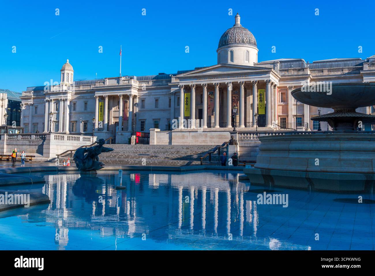 London, England, Großbritannien - 10. Mai 2025: Blick auf die National Gallery am Trafalgar Square spiegelt sich früh im blauen Wasser des Brunnens wieder Stockfoto