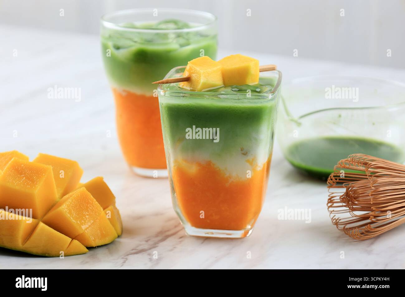 Iced Mango Matcha Latte in Glas auf weißem Tisch Stockfoto