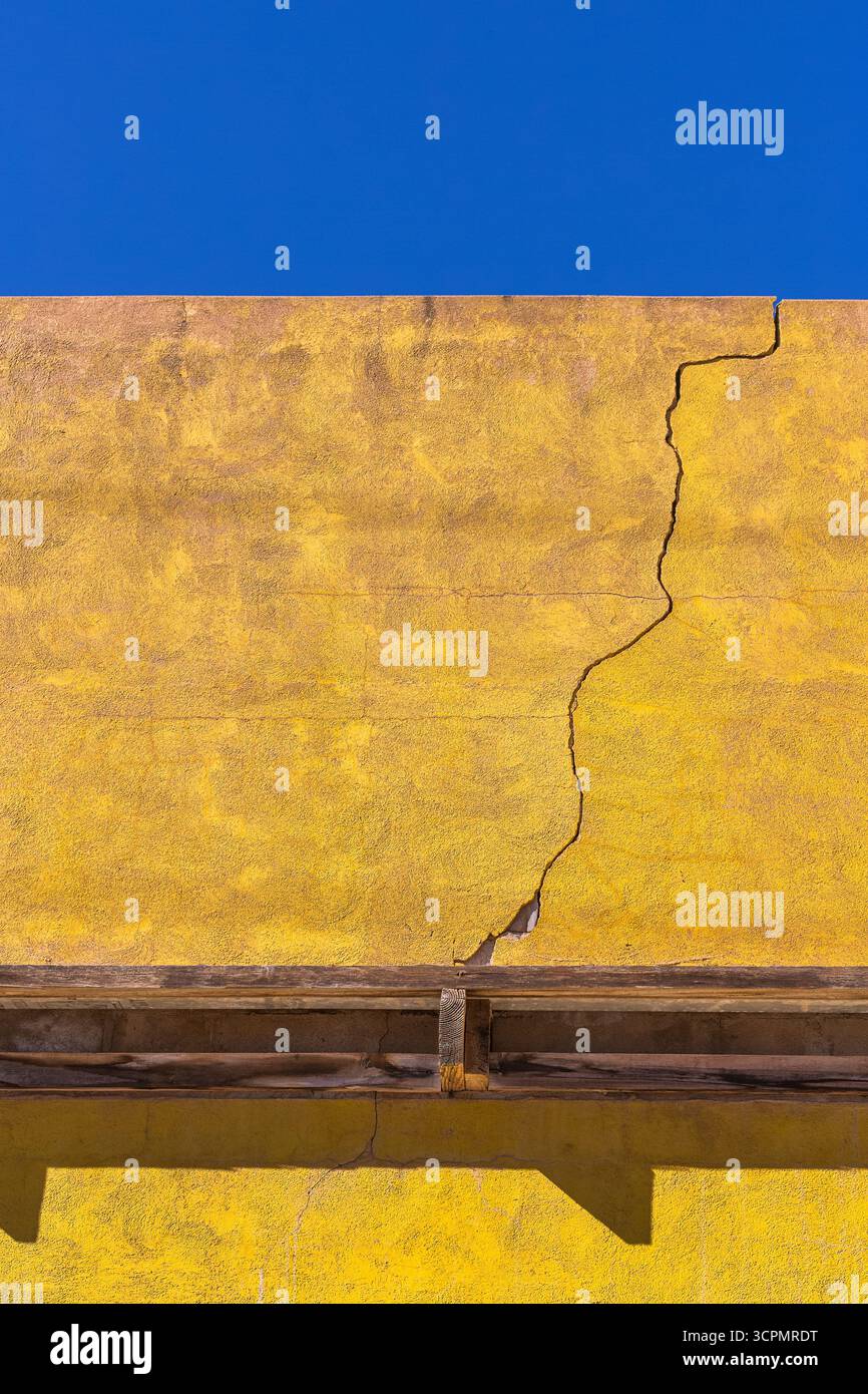 Eine gelb gerenderte Wand unter einem leuchtend blauen Himmel. Die Oberfläche weist einen auffälligen vertikalen Riss auf, der auf Verschleiß hinweist. Stockfoto