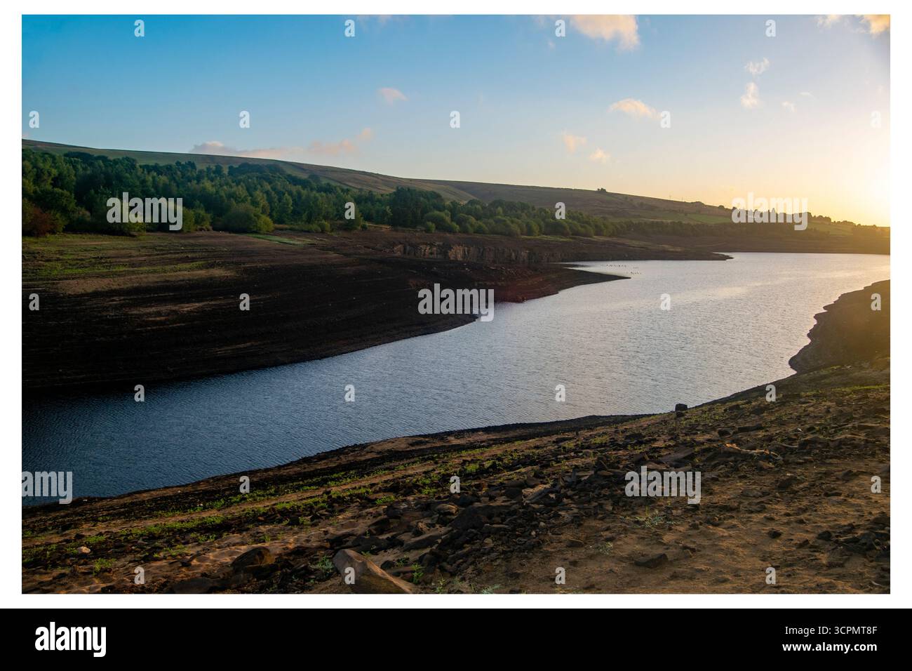 Das Morgenlicht beleuchtet das stark erschöpfte Baitings Reservoir und offenbart weite, durch die anhaltende Dürre ausgelöste Flächen. Stockfoto