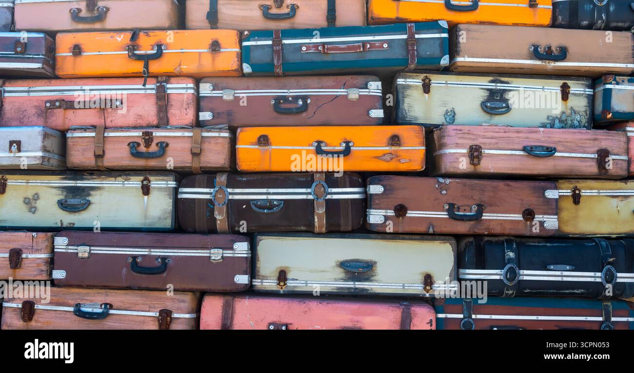 Eine Kollektion farbenfroher Vintage-Koffer ist vor einem Hintergrund gestapelt und sorgt für eine auffällige visuelle Präsentation auf einem Markt im Freien. Heller Sonnenschein Stockfoto