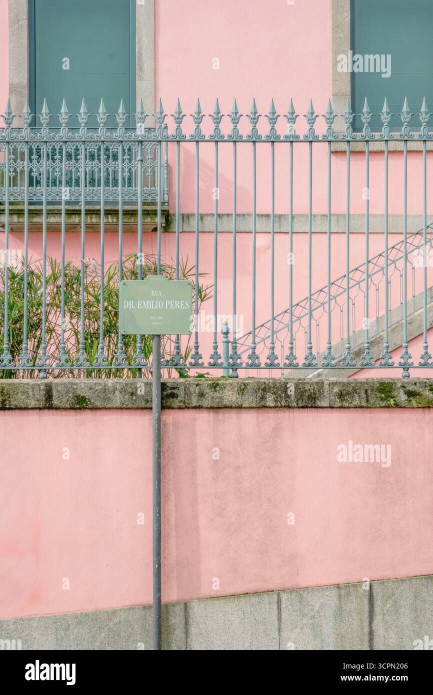 Wand In Pastellrosa Mit Dekorativem Grauem Metallzaun Und Straßenschild. Städtische Ästhetik, Architektur, Weiche Farbpalette, Architektonische Texturen Stockfoto