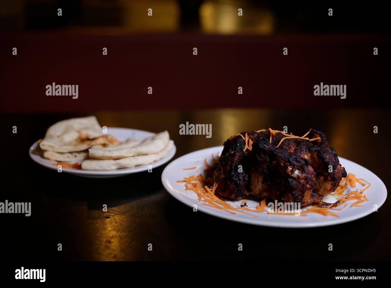 Dunkel geröstetes oder gegrilltes Tandoori-Hühnchen mit Naan-Brot in einem Restaurant Stockfoto