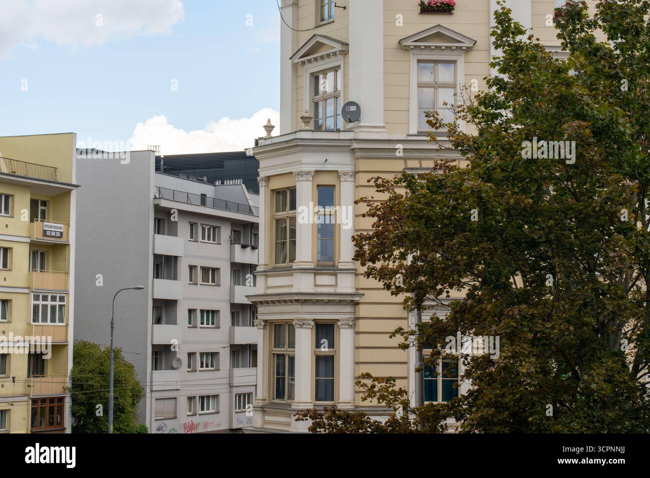 Kontrast zu neoklassizistischem cremefarbenem Gebäude mit kunstvollen Säulen und modernem weißen Apartmentblock unter blauem bewölktem Himmel. Konzept der architektonischen Vielfalt Stockfoto