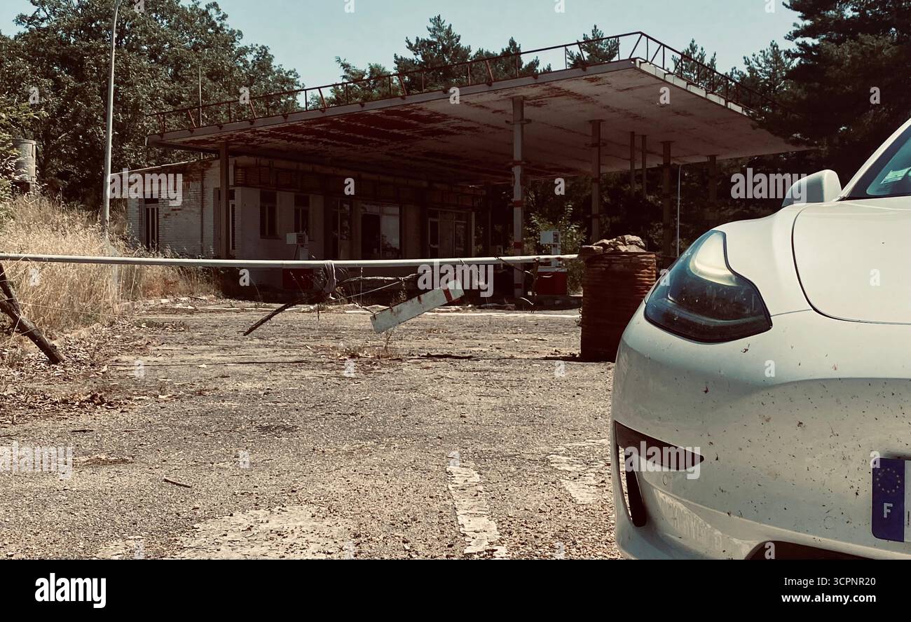 Modernes Auto vor einer verlassenen Tankstelle, umgeben von Wald - Smartphone-aufgenommenes Stockfoto