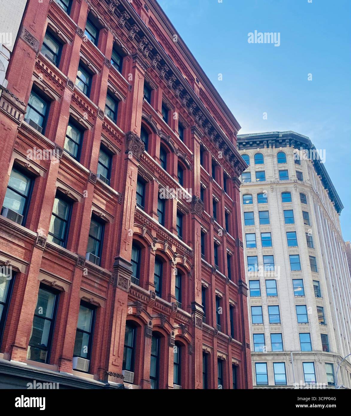 Kontrastreiche städtische Gebäude mit Ziegelfassade und moderner Architektur unter blauem Himmel Stockfoto