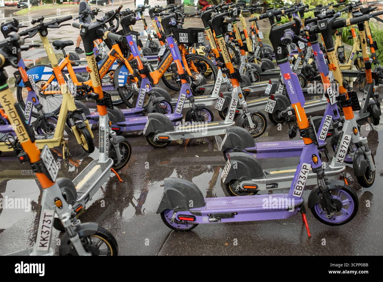 25. August 2025, Moskau, Russland. Mehrere Elektroroller parken ordentlich auf einem nassen Gehweg nach einem Regenschauer und sind hell Stockfoto
