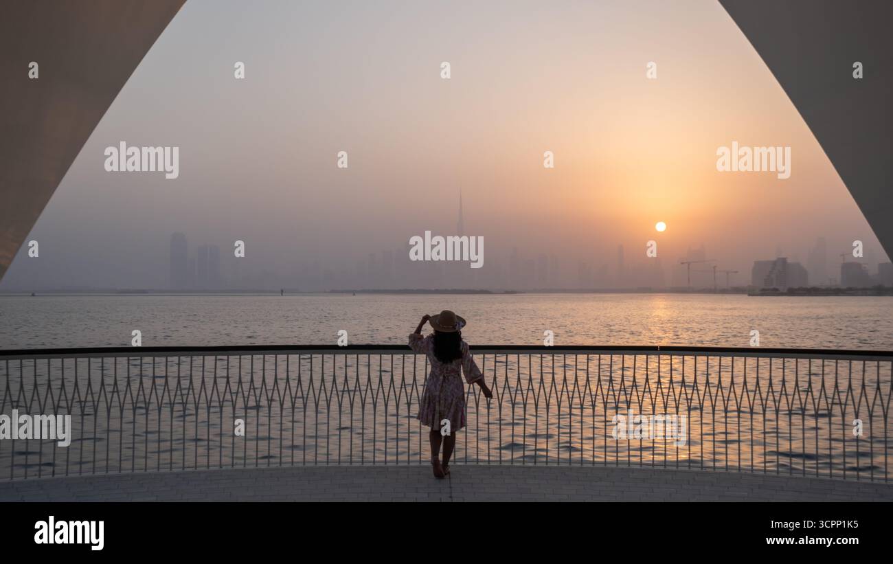 Silhouette eines Mädchens, das die Skyline von Dubai zur goldenen Stunde bewundert, malerischer Blick vom Hafen von Dubai Creek im Winter - horizontales Stockfoto Stockfoto